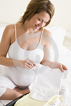 Pregnant woman packing baby clothing in suitcase