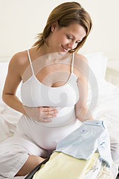 Pregnant woman packing baby clothing in suitcase