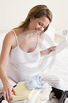 Pregnant woman packing baby clothing in suitcaseh