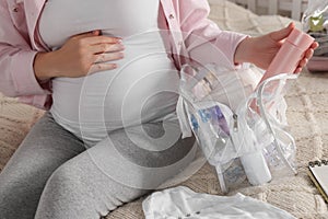 Pregnant woman packing baby stuff to bring into maternity hospital in bedroom, closeup