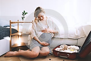 Pregnant woman is packing suitcase for maternity hospital getting ready for childbirth. Happy young mother with travel luggage of