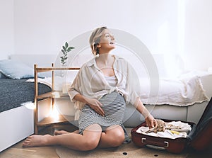 Pregnant woman is packing suitcase for maternity hospital getting ready for childbirth. Happy young mother with travel luggage of