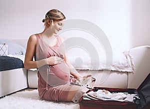 Pregnant woman is packing suitcase for maternity hospital getting ready for childbirth. Happy young mother with travel luggage of