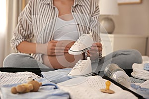 Pregnant woman packing suitcase for maternity hospital at home, closeup