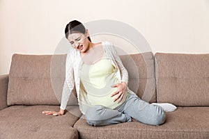 Pregnant woman with painful belly on sofa at home