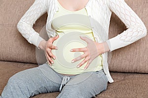 Pregnant woman with painful belly on sofa at home