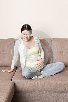 Pregnant woman with painful belly on sofa at home