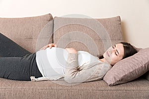 Pregnant woman with painful belly on sofa at home