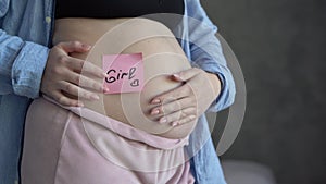 Pregnant woman with paper sticker on tummy with inscription girl. Concept of choosing baby name, pregnancy woman problem