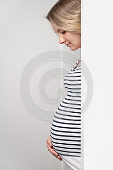 Pregnant woman peeking out of white wall