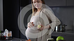 A pregnant woman peels onions with a kitchen knife and communicates using a mobile phone while standing near the table