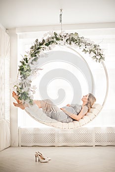 Pregnant woman in peignoir with swings that are decorated for the New Year close-up. A woman waiting for a baby in a silver dress