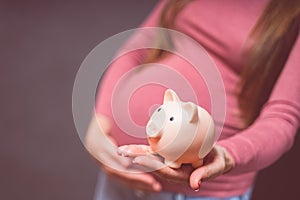 Pregnant woman with piggy bank, saving money to her newborn baby.