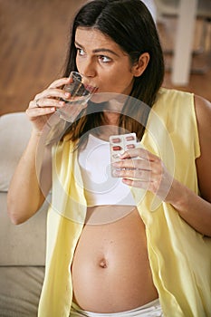 Pregnant woman with pill and drinking glass.