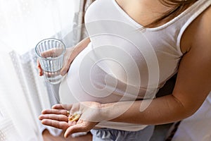 Pregnant woman pills vitamin. Happy smiling woman taking pill with supplement vitamin Omega 3. Vitamin D, E, A Fish Oil