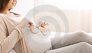 Pregnant woman playing with tiny shoes, stepping on belly