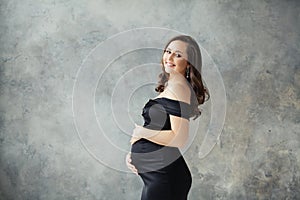 Pregnant woman portrait. Beautiful lady wearing black dress smiling