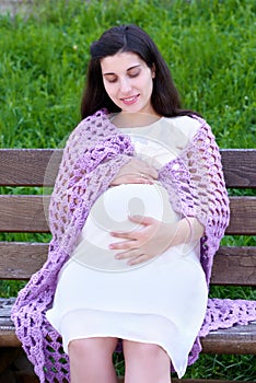 Pregnant woman portrait on outdoor, happy maternity concept, sit on bench in city park, summer season, green grass background