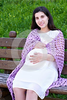 Pregnant woman portrait on outdoor, happy maternity concept, sit on bench in city park, summer season, green grass background