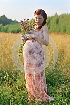 Pregnant woman poses with wild flowers at summer day outd