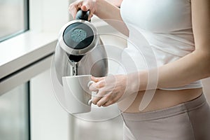 Pregnant woman pouring water from electric kettle