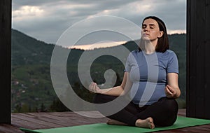 Pregnant woman practicing meditation outdoor on a terrace with mountain view