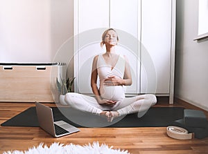 Pregnant woman practicing yoga online at home with laptop