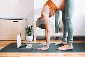 Pregnant woman practicing yoga online at home with laptop