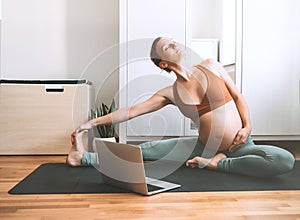 Pregnant woman practicing yoga online at home with laptop