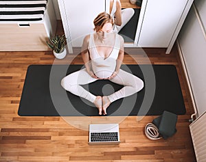 Pregnant woman practicing yoga online at home with laptop