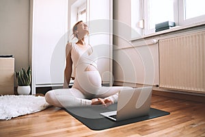 Pregnant woman practicing yoga online at home with laptop