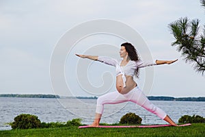Pregnant woman is practicing yoga beside river