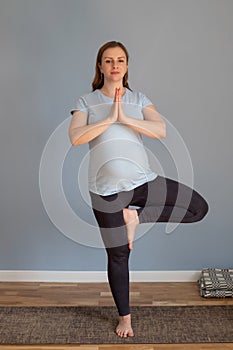 Pregnant woman practicing yoga, standing in tree pose or vriksasana