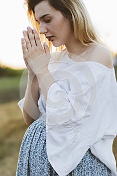 Pregnant woman praying outdoors on at sunset. Concept for faith, spirituality and religion.