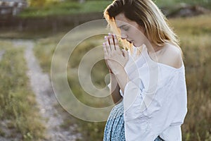 Pregnant woman praying outdoors on at sunset. Concept for faith, spirituality and religion.