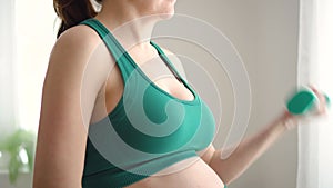 A pregnant woman prepare for exercising with dumbbells. Young girl holding a yoga mat in hand.