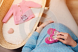 Pregnant woman preparing for baby birth her daughter. Happy mother enjoying pregnancy. Wicker basket of cute tiny stuff newborn