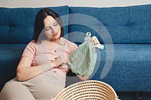 Pregnant woman preparing for baby birth her daughter. Happy mother enjoying pregnancy. Wicker basket of cute tiny stuff newborn