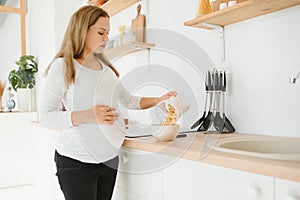 Pregnant woman preparing breakfast, cereals with milk and natural juice, in the kitchen