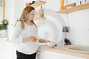 Pregnant woman preparing breakfast, cereals with milk and natural juice, in the kitchen