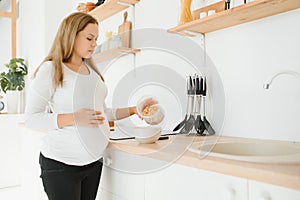 Pregnant woman preparing breakfast, cereals with milk and natural juice, in the kitchen