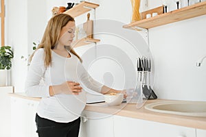 Pregnant woman preparing breakfast, cereals with milk and natural juice, in the kitchen