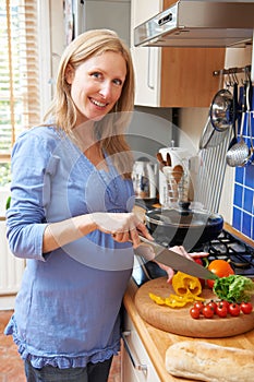 Pregnant Woman Preparing Meal In Kitchen