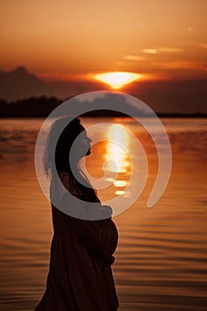 Pregnant woman in profile at sunset. Side view of silhouette in rays of setting sun reflected in water of beautiful