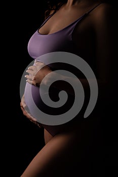 A pregnant woman in a purpule bodysuit put her hands on her stomach, close-up. Expecting a baby.