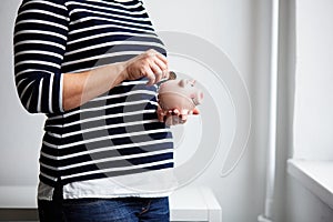 Pregnant woman putting coin into small piggy bank