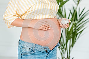 Pregnant woman putting sunscreen on her belly. Close up, isolated