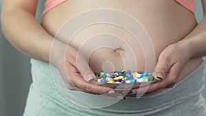 Pregnant woman putting up bowl with pills, making refusal gesture, no medication