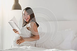 Pregnant woman reading a book on a bed at home