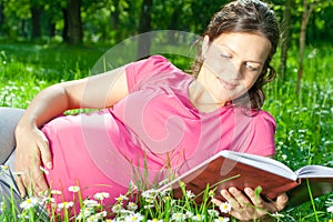 Pregnant woman reading book on grass